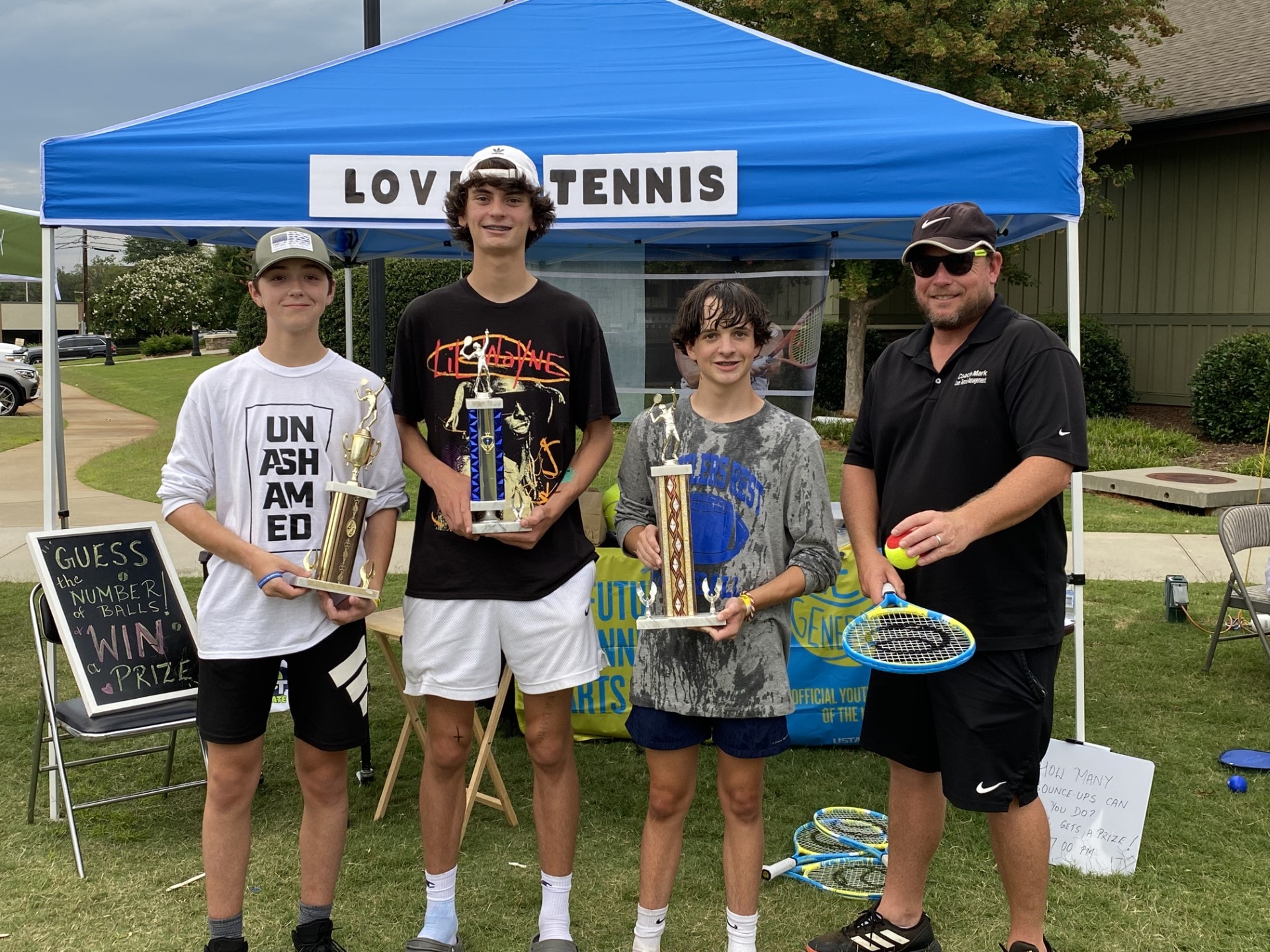 Young players holding trophies under the Love Tennis tent at a GTL tournament event