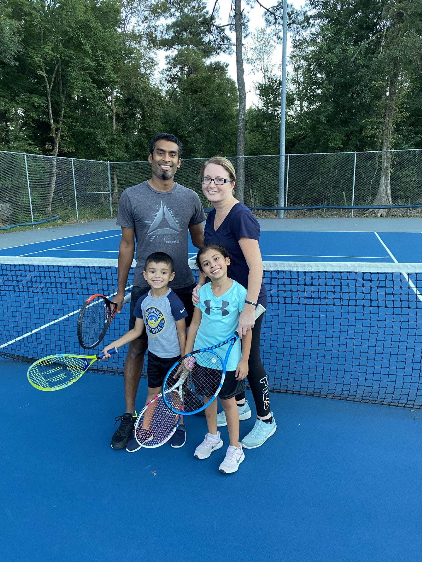A family of four smiling at the net after a tennis lesson