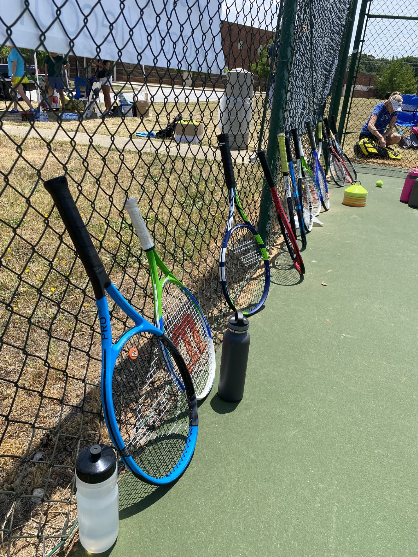 Tennis rackets and water bottles lined up along the court fence at a GTL event