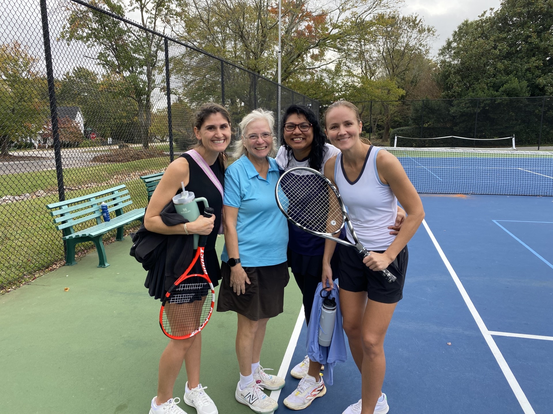 Four adults smiling together on the tennis court after a group session