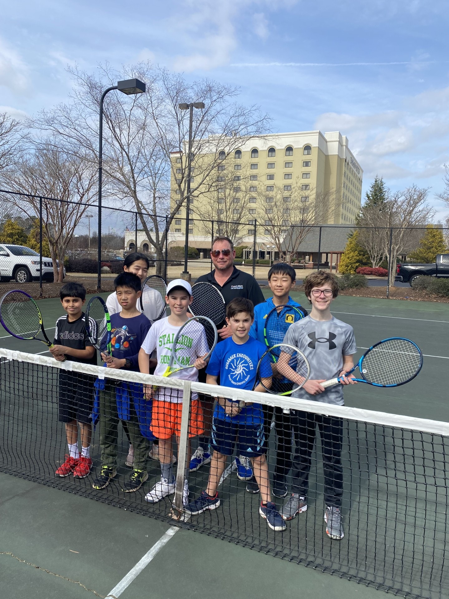 Mark and a group of junior players posing at the net after a lesson